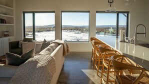 Una cucina moderna con una grande isola, sedie in legno e vista su un paesaggio innevato attraverso ampie finestre.