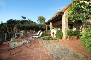 Une terrasse avec un sol en pierre, une pergola et un espace détente avec des fauteuils.