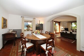 A dining area with a round wooden table, six chairs, a vase of flowers, and a painting on the wall.