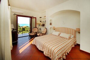 A bedroom with a large bed, a chair, a desk, and a view of the ocean.