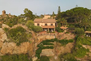 A Mediterranean-style villa with a terracotta roof, surrounded by lush greenery and rocky terrain.