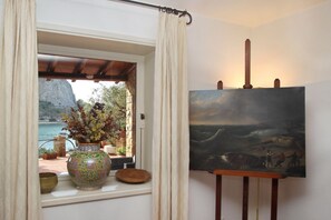 Une pièce avec une grande fenêtre, un tableau accroché au mur et un vase rempli de fleurs posé sur le rebord de la fenêtre.