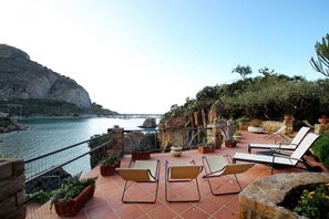 A terrace with sun loungers overlooking a coastal area with cliffs and a body of water.