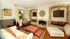 A cozy living room with a fireplace, a sofa, a coffee table, and a stone fireplace surround. - Villa Faraglioni – Private Beach in Cefalù (Cefalù)