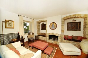 A cozy living room with a fireplace, a sofa, a coffee table, and a stone fireplace surround. - Villa Faraglioni – Private Beach in Cefalù (Cefalù)