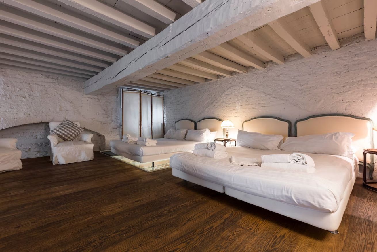 A bedroom with two beds, wooden flooring, and a rustic stone wall.