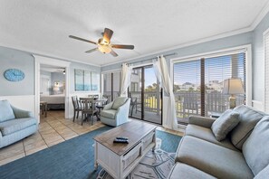 Ein großzügiges Wohnzimmer mit Deckenventilator, einer Couch, einem Couchtisch und Blick auf die Stadt durch große Fenster.