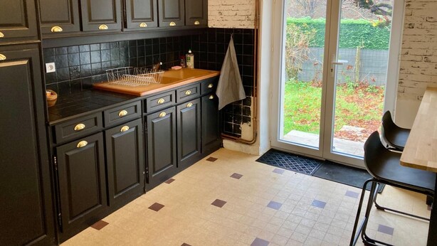 Une cuisine avec des meubles de couleur sombre, un plan de travail en bois et une vue sur un jardin, accessible par une porte-fenêtre coulissante.