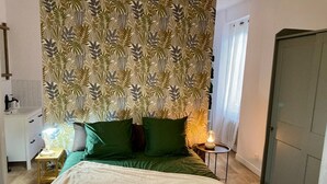 Une chambre à coucher avec un lit, des coussins verts, une lampe de chevet et un papier peint à motifs.