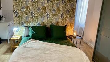Een slaapkamer met een bed, groene kussens, een bedlamp en behang met een patroon.