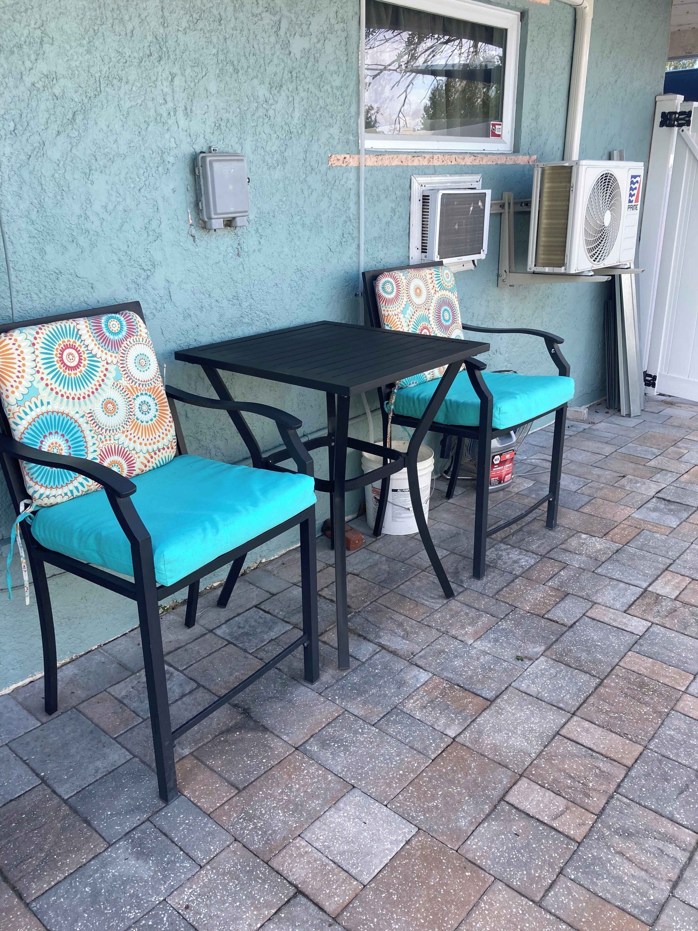 An outdoor patio with two black metal tables and chairs, each with colorful patterned cushions.