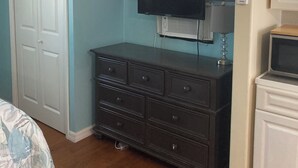 Quarto com cama, cômoda, televisão, ar condicionado e janela com cortinas.