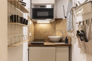 A compact kitchen with a built-in oven, a white sink, and a shelf with dishes. - Ghibellina Comfort Apartment (Firenze)