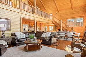 Ein geräumiges Blockhaus-Interieur mit Wohnbereich, Essbereich und einer Treppe zu einer oberen Galerie.