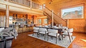 Una cabaña de madera espaciosa con comedor, cocina y una escalera que sube a un altillo.
