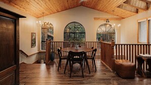 Un'area da pranzo con pavimento in legno, un tavolo rotondo e sedie, una ringhiera in legno e una ventola a soffitto.