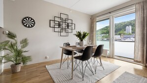 Een eethoek met een tafel voor vier personen, een potplant, een dartbord en een modern kunstwerk aan de muur.