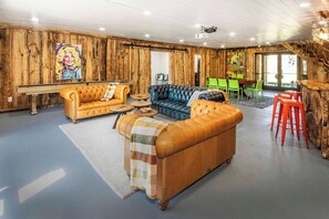 A room with wooden walls, a large sofa, a smaller sofa, a coffee table, and a bar area with stools. - Riverfront Barndominium, Incredible Outdoor Space! (Townsend)