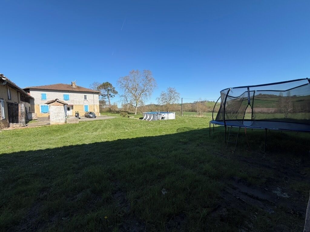 En græsplæne med trampolin, et hus og et lille skur.