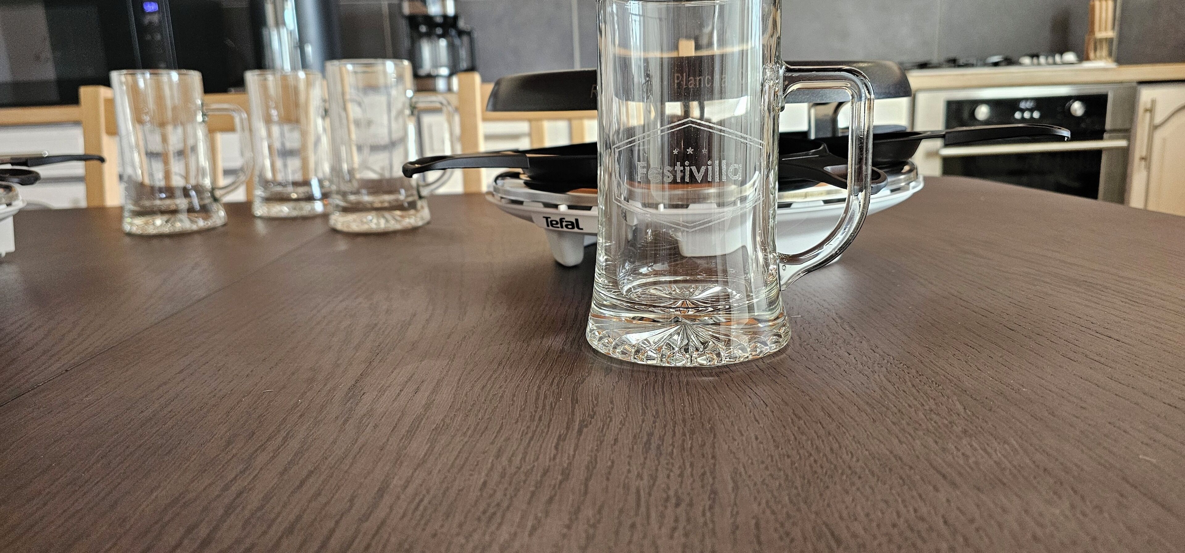 Una taza de vidrio transparente con asa sobre una mesa de madera, rodeada de otras tazas de vidrio transparente.