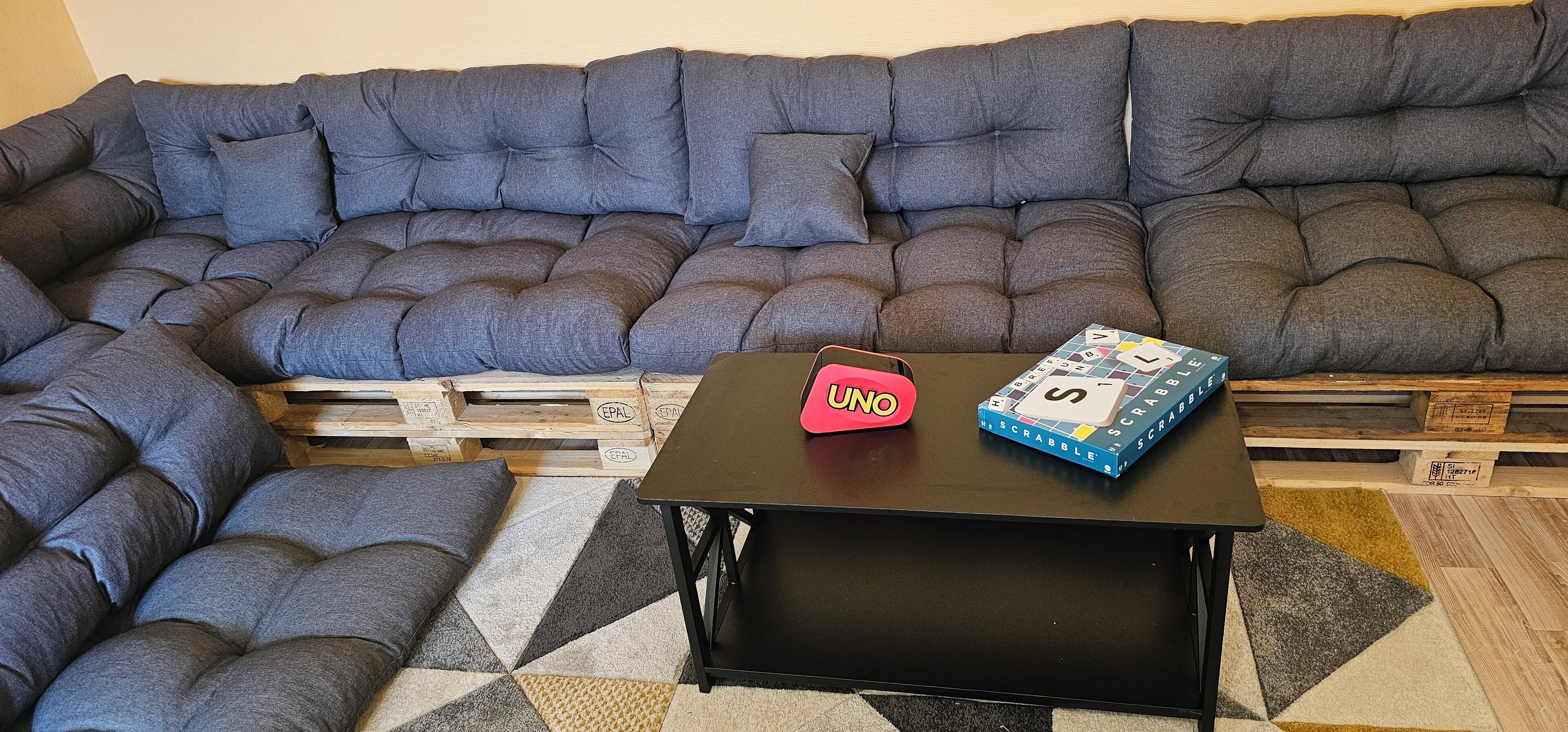 Un canapé modulable avec une base en bois, une table basse noire et une boîte de jeu de Scrabble.