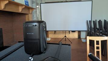 Un proyector sobre una mesa con una pantalla en blanco al fondo.
