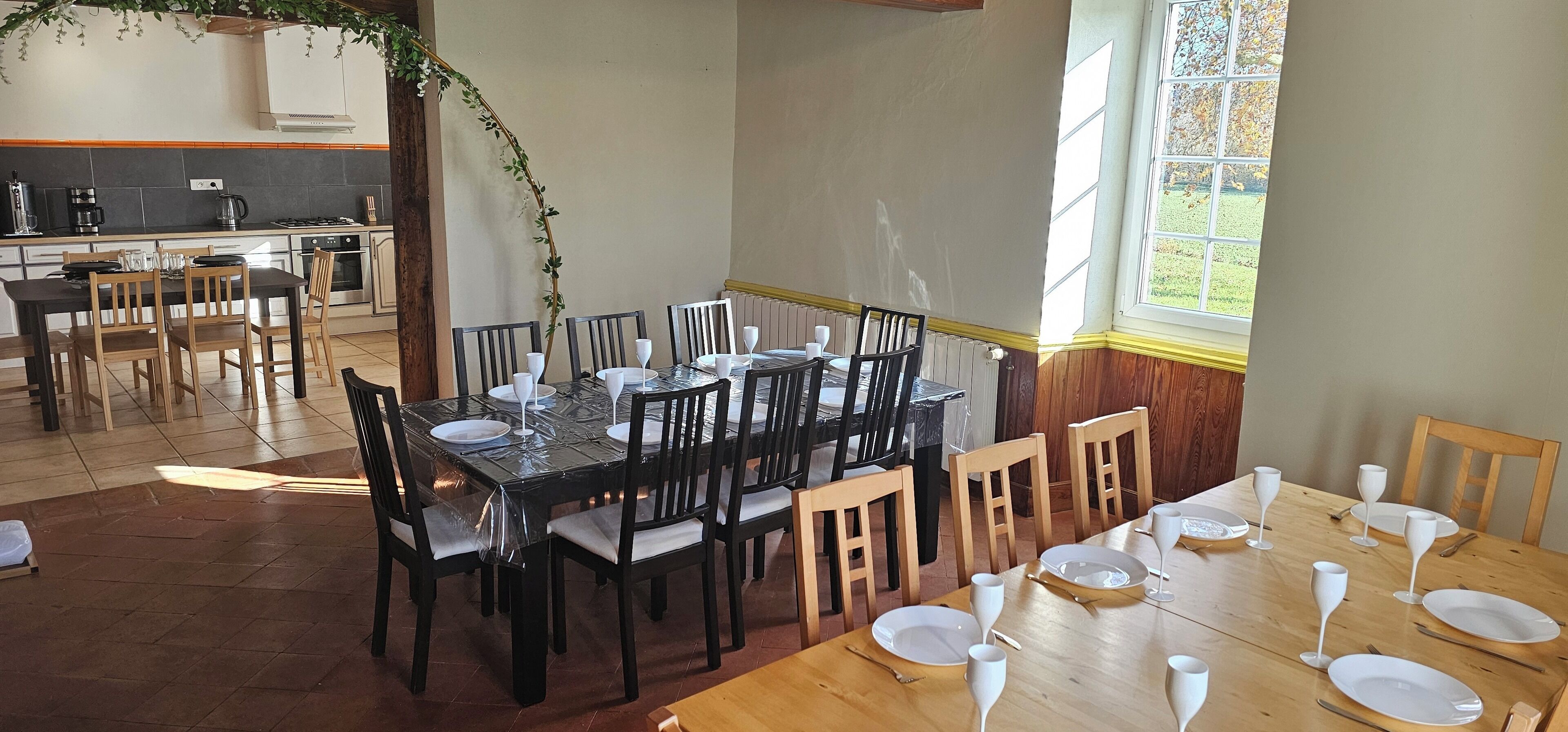 Un comedor con una mesa grande dispuesta para seis personas, rodeada de sillas de madera. Se ve una cocina al fondo con electrodomésticos modernos.