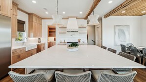 A modern kitchen with a large island, wooden cabinets, and hanging pendant lights. - Crabstar|Easy Beach Access|Private Pool & Golf Cart (Inlet Beach)