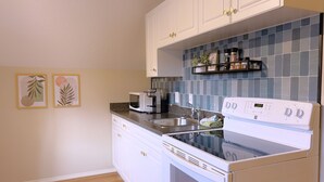 Una cocina con armarios blancos, un microondas, una estufa y un fregadero. Hay dos cuadros en la pared.
