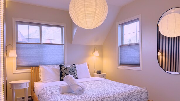 Un dormitorio con cama, mesitas de noche, lámparas y un ventanal grande.