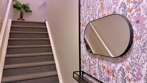 Una escalera con peldaños alfombrados, un espejo fijado a la pared y un papel tapiz con motivos florales.