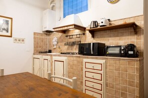 Une cuisine avec des meubles blancs, une table en bois et un revêtement mural en carreaux.