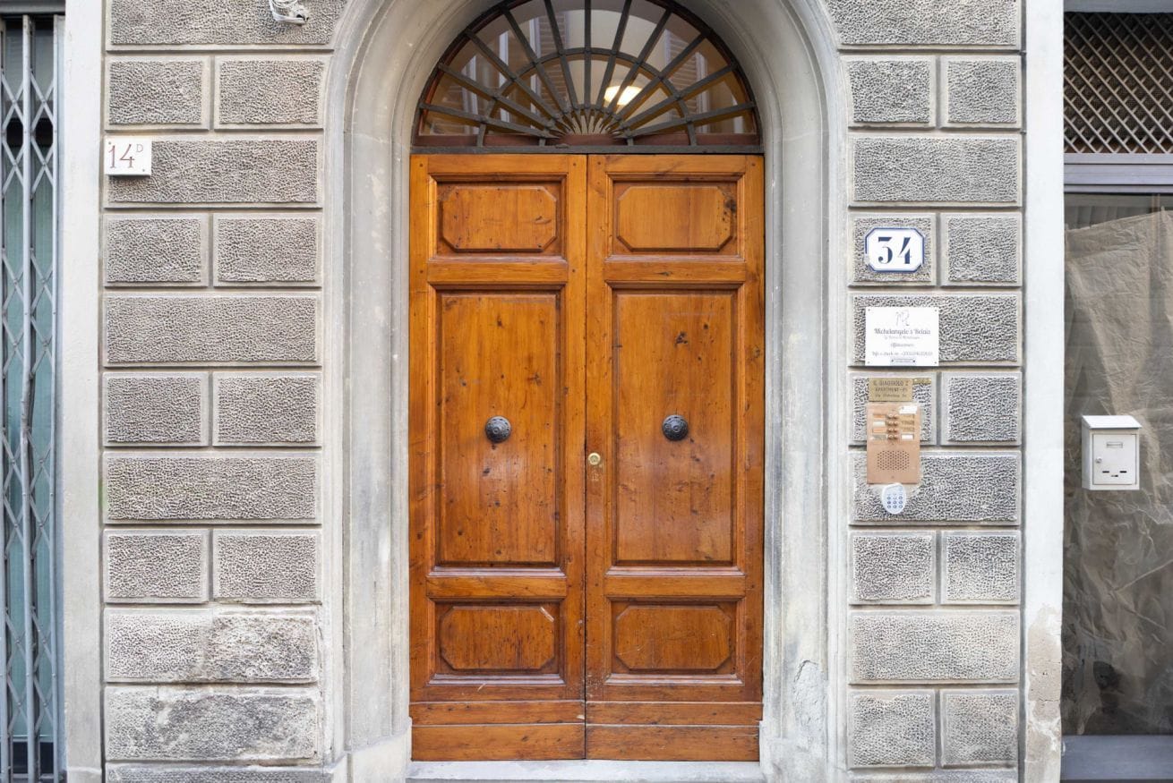 A wooden double door with a fanlight above it, set in a stone wall with numbered plaques.