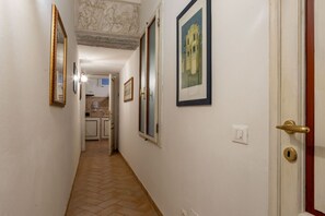 Un couloir doté d’un sol carrelé, une porte avec une poignée en laiton et des tableaux encadrés accrochés aux murs.