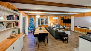 A cozy, well-lit living room with wooden walls and a dining area featuring a wooden table and chairs. - Spacious Luxe-Lodge 5br Lakefront (Greenfield)