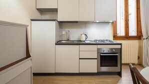Een compacte keuken met witte kastjes, een gasfornuis, een waterkoker en een inbouwoven.