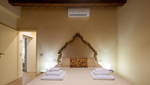 Een hotelkamer met een groot bed, twee nachtkastjes, een airconditioning en een deur naar een andere kamer.