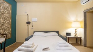Een hotelkamer met een bed, een bureau, een stoel, een lamp en een wandairconditioner.