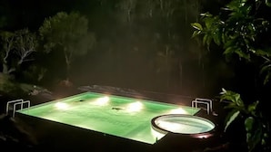 Piscina exterior de noche con árboles circundantes y cielo oscuro.