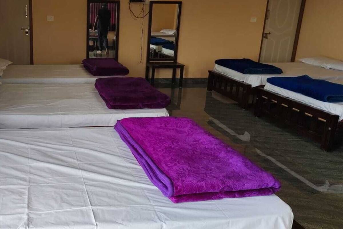 A hotel room with four beds arranged in a row, each with white bedding and purple blankets.