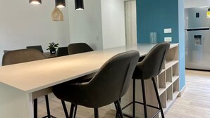Una cocina moderna con refrigerador empotrado, comedor con mesa larga y sillas, e iluminación colgante.