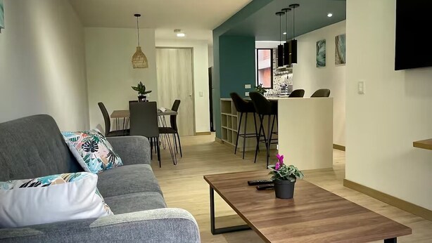 Una sala de estar moderna con un sofá gris, una mesa de centro de madera y un comedor con una mesa y sillas.