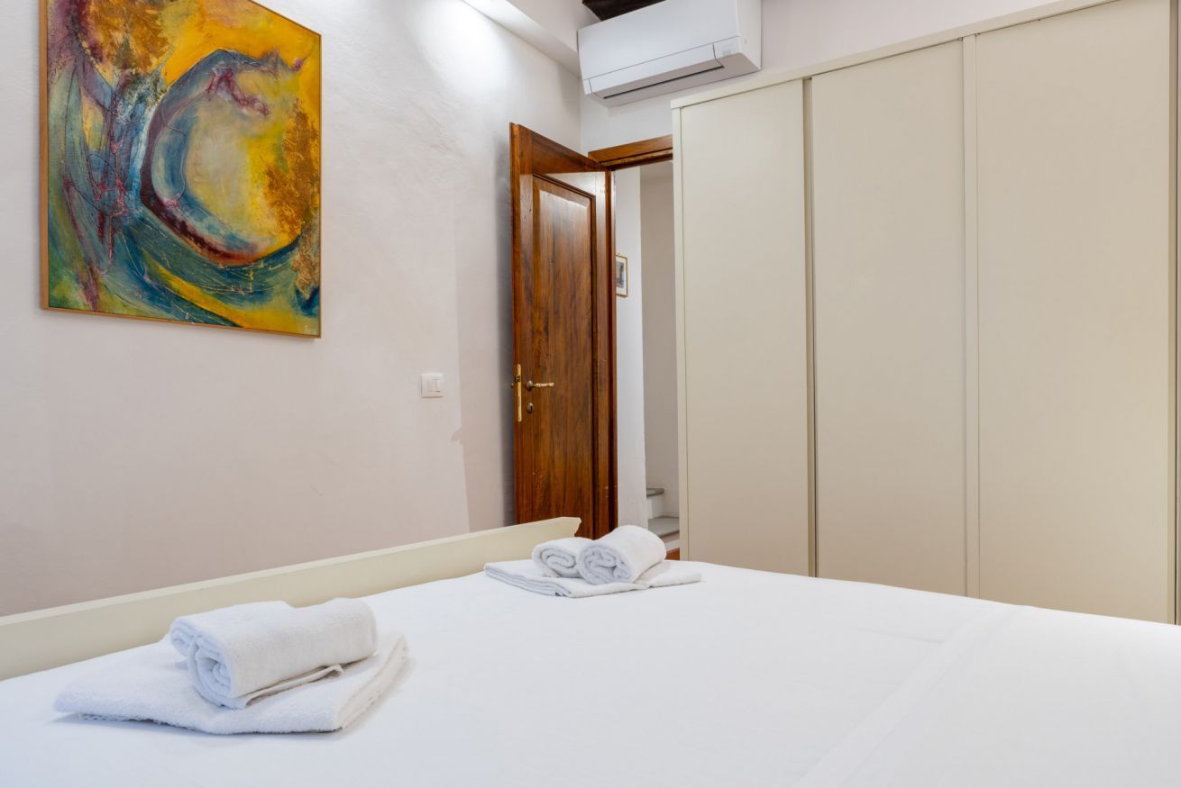 A hotel room with a bed, a painting on the wall, and a wardrobe.