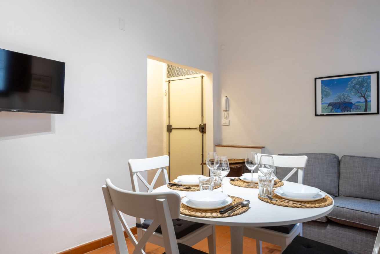 Un coin repas avec une table ronde pour quatre personnes, des chaises blanches et un téléviseur à écran plat fixé au mur.