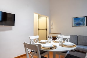 A dining area with a round table set for four, white chairs, and a flat-screen TV mounted on the wall. - Bargello Apartment - Florence City Center  (Firenze)