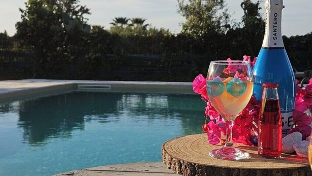 Escena junto a la piscina con una botella de vino Cerasolella, una copa de cóctel y una alfombra decorativa con el texto "Villa Cerasolella".