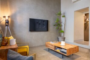 A modern living room with a large flat-screen TV mounted on the wall, a wooden coffee table with books and a candle, a yellow chair, and a potted plant. - CHIESA 12 3P - Florence (Firenze)