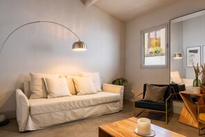 A modern living room with a white sofa, a wooden coffee table with a candle, a blue armchair, and a large window with plants. - CHIESA 12 3P - Florence (Firenze)