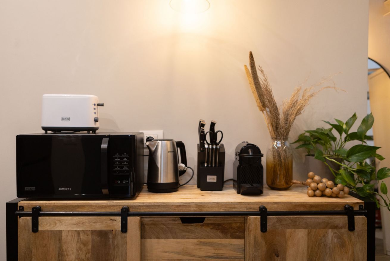 Una encimera de cocina con microondas, cafetera y utensilios.
