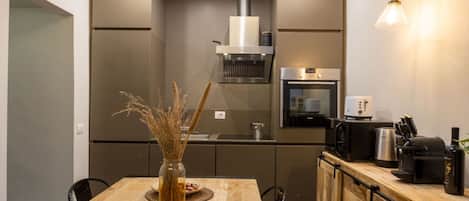 Una cocina moderna con una mesa de comedor de madera, horno empotrado y una cafetera.